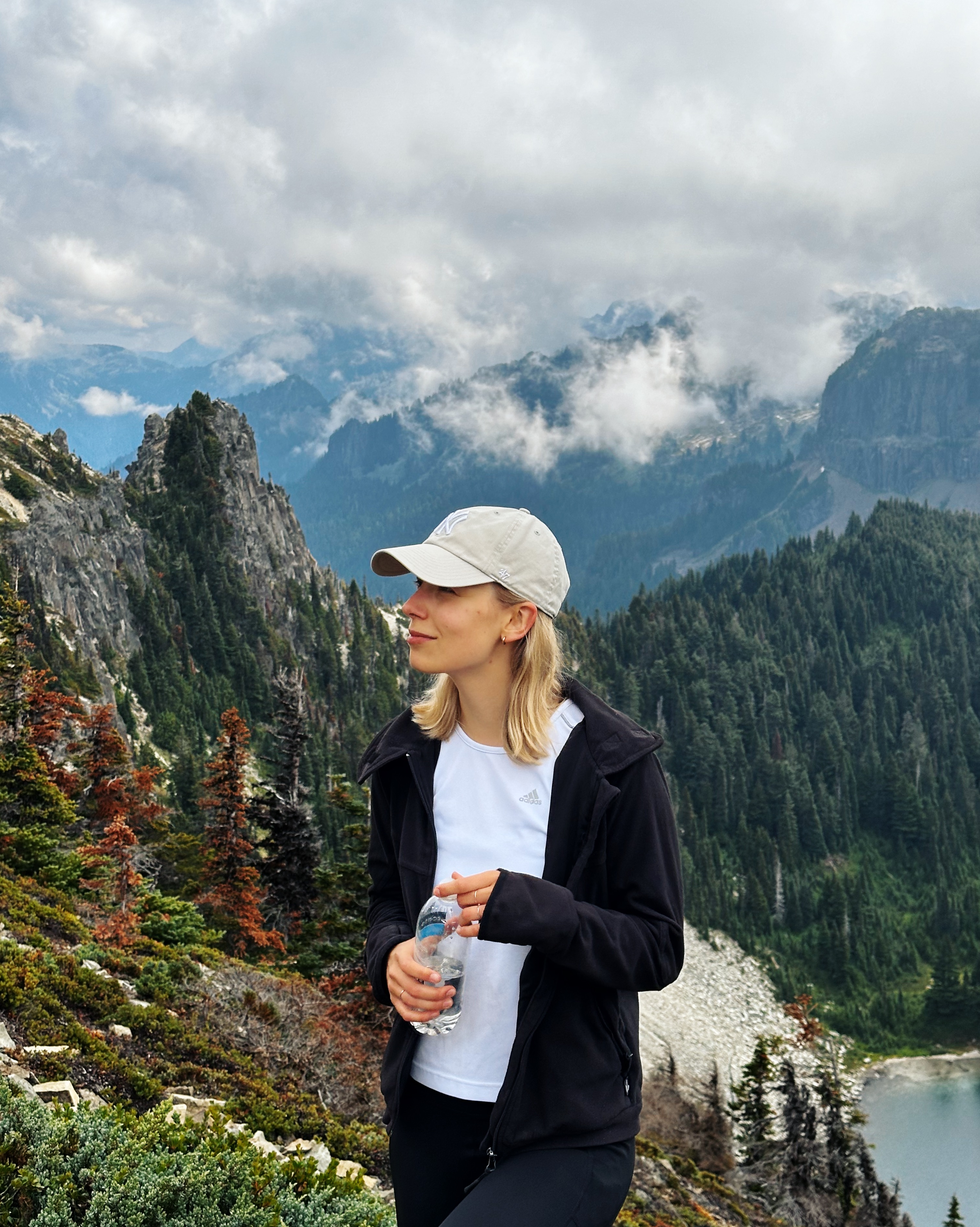 Girl in a cap with a bottle of water in front of a mountain ridge.