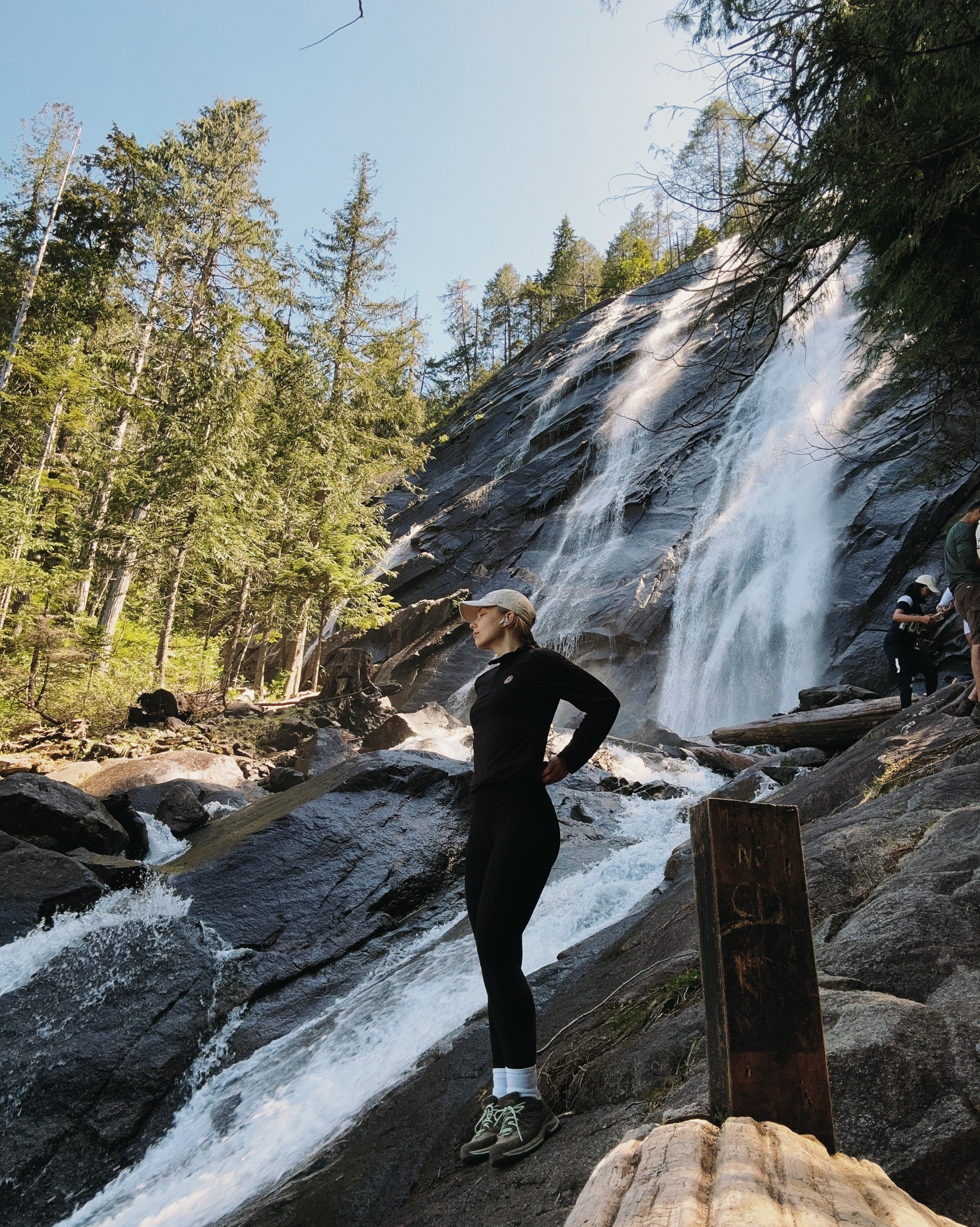 Girl in hiking attire standing in front of the rocky waterfall.