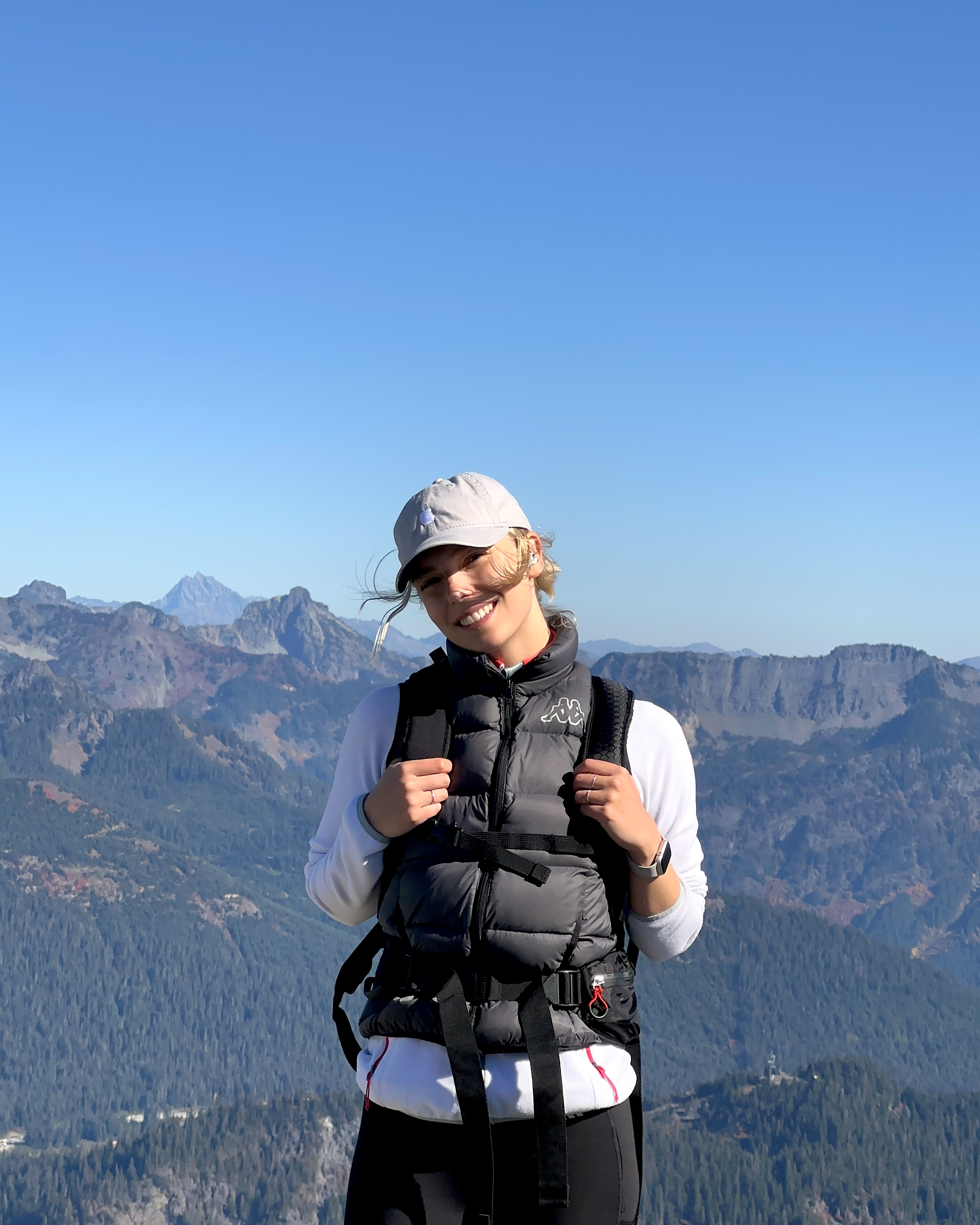 Girl with a hiking backpack smiling in front of the mountain ridge 